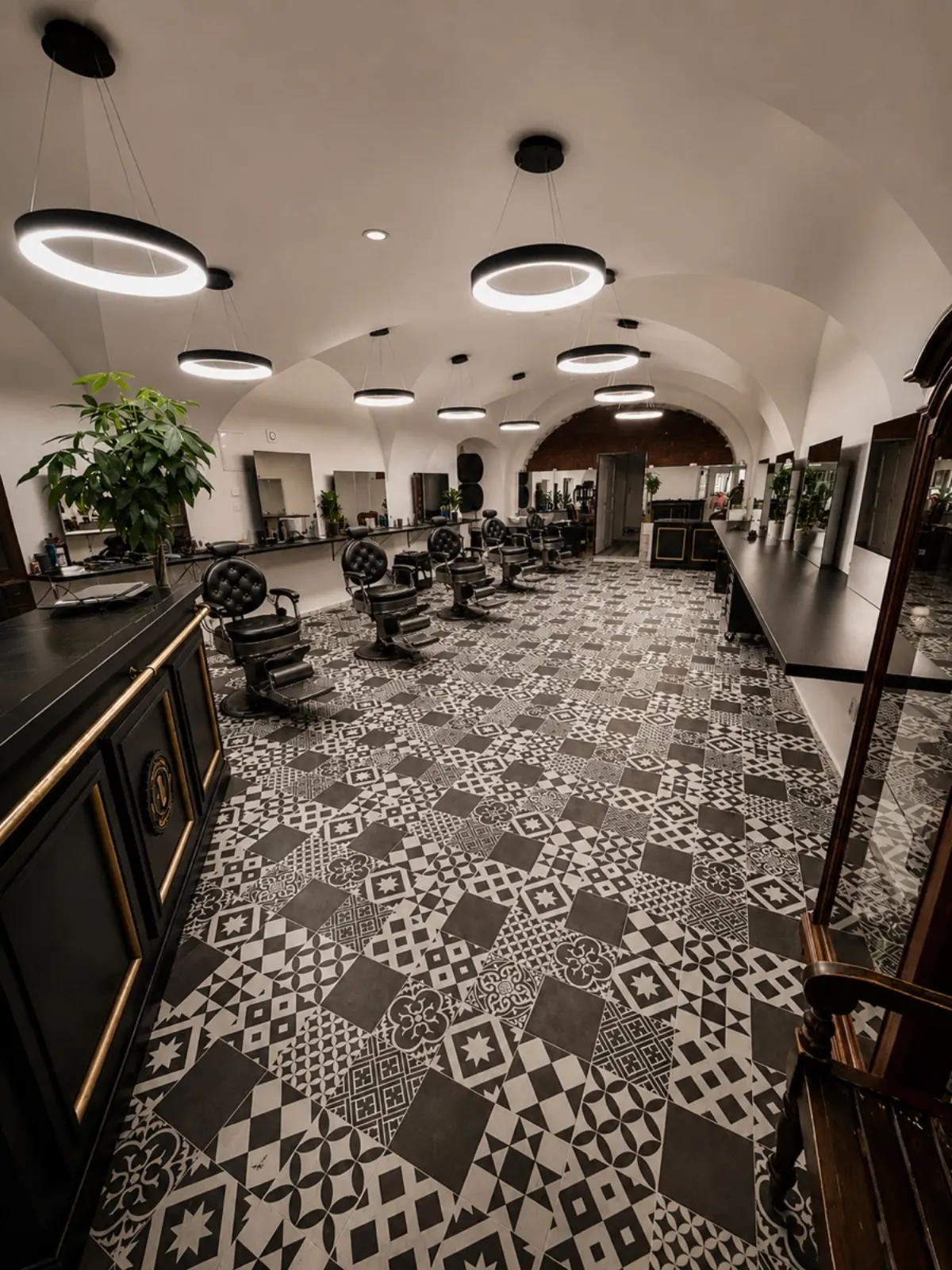 Interiér Elite Barbershopu, klenutý strop, kruhové lampy, cementové dlaždice, kožené barber chairs
